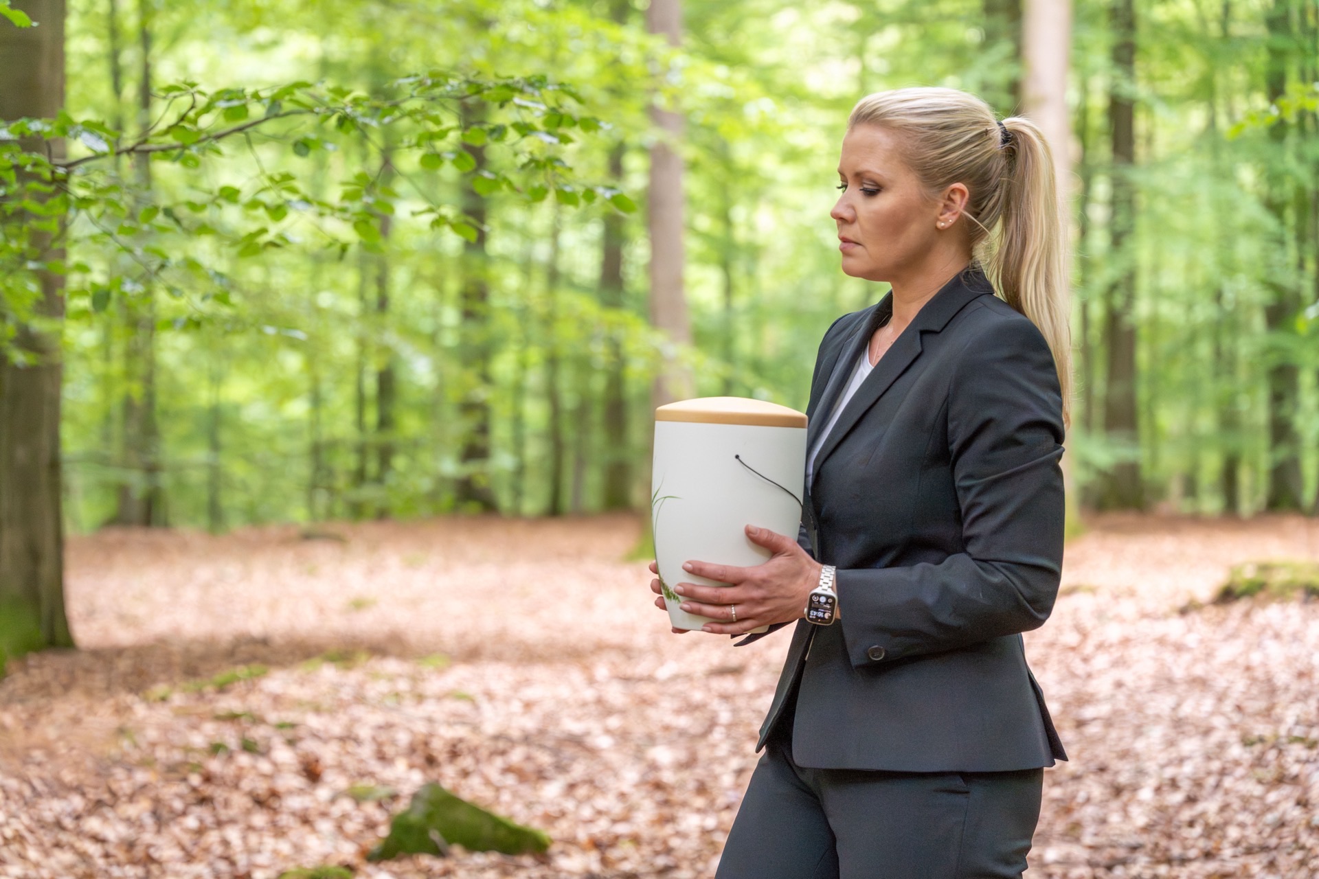Bestatterin trägt eine Urne im Wald