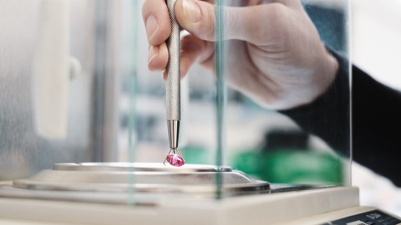 Edelstein wird mit einer Pinzette auf einer Feinwaage abgewogen